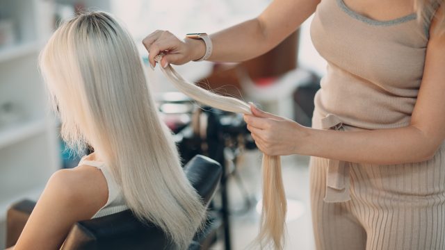 Hairdresser female making hair extensions to young woman with blonde hair in beauty salon. Professional hair extension.